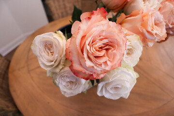A close-up view of a bouquet featuring a mix of delicate orange and white roses, arranged elegantly on a wooden table with soft lighting enhancing the intricate petal details.