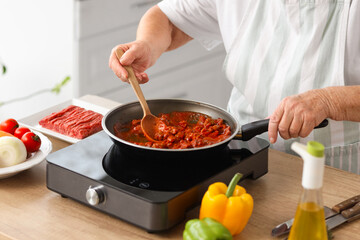 Senior woman frying food in kitchen, closeup