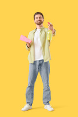 Handsome man with rag and detergent on yellow background