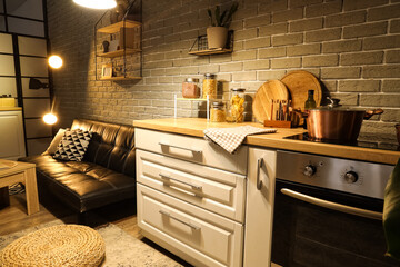 Interior of kitchen with counters, sofa and glowing lamps in evening