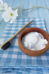 A wooden bowl of baking soda, a bamboo toothbrush, and a glass jar on a fabric