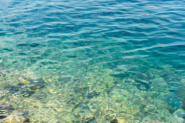Close-up of crystal-clear turquoise sea water with shimmering sunlight reflections and underwater stones. Concept of tropical paradise, aquatic purity, and peaceful natural beauty.