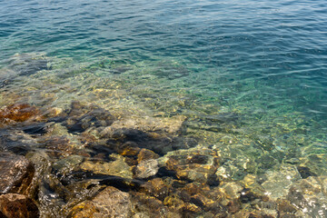Transparent turquoise sea water with sunlit rocky coast on a bright summer day. Concept of serene marine scenery, coastal charm, and unspoiled natural beauty.