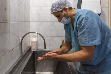 Latino medical worker washing his hands in a stainless steel sink in a sterile hospital environment.