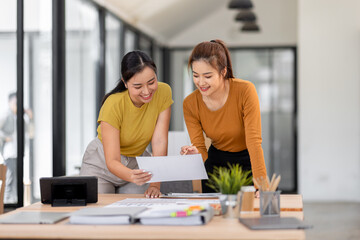 Happy two asian female freelance entrepreneurs reading and planning analyzing the financial report, business plan investment,  on computer while working together in the office.
