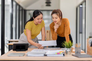 Fototapeta premium Happy two asian female freelance entrepreneurs reading and planning analyzing the financial report, business plan investment, on computer while working together in the office. 