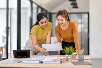 Obraz premium Happy two asian female freelance entrepreneurs reading and planning analyzing the financial report, business plan investment, on computer while working together in the office. 