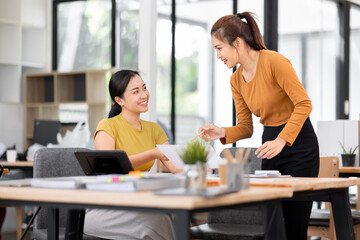 Happy two asian female freelance entrepreneurs reading and planning analyzing the financial report, business plan investment,  on computer while working together in the office.

