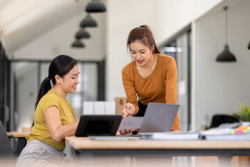 Fototapeta premium Happy two asian female freelance entrepreneurs reading and planning analyzing the financial report, business plan investment, on computer while working together in the office. 