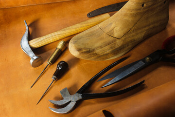 shoe last and shoe making tools on a sheet of leather which also serves as a background