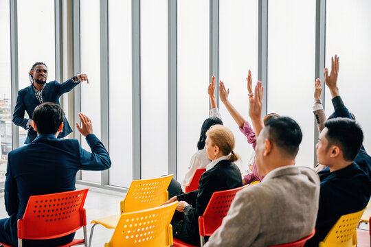 Businesspeople gather at a corporate event for a conference and convention. Raised hands symbolize questions and voting reflecting active participation in a meeting training seminar and discussions.