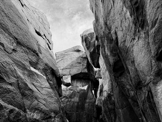 A black-and-white image of towering rock formations forming a narrow passage, highlighting rugged textures and natural erosion.