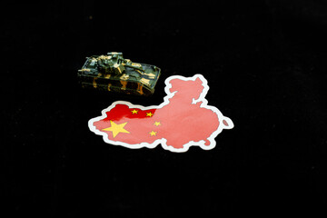 Military toy tank on China map flag isolated on black background.