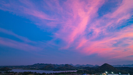 A panoramic view of dramatic mountain peaks silhouetted against a vibrant sunset sky, with fiery hues of red, orange, and pink blending into the fading blue. sunflowers fields around the mountains.