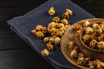 Caramelized popcorn in a wooden bowl with a plate on a wooden background
