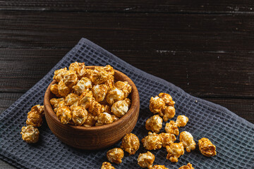 Caramelized popcorn in a wooden bowl with a plate on a wooden background