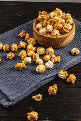 Snack concept, sweet caramelized popcorn in a wooden bowl on a black background