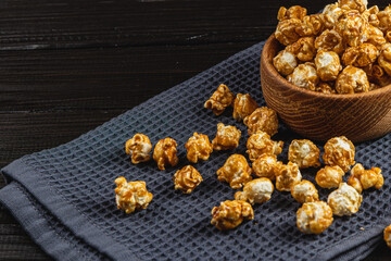 Caramelized popcorn in a wooden bowl with a plate on a wooden background