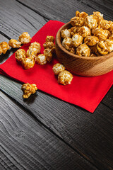 Snack, movie concept, caramelized popcorn in a wooden bowl on a red napkin