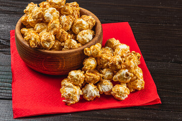 Snack, movie concept, caramelized popcorn in a wooden bowl on a red napkin