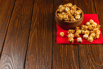 Snack, movie concept, caramelized popcorn in a wooden bowl on a red napkin