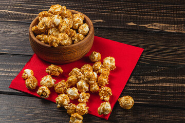 Caramelized popcorn in a wooden bowl on a red napkin on a wooden table