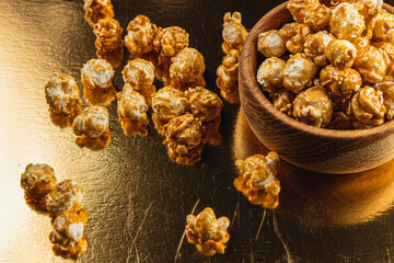 Sweet caramelized popcorn in a wooden bowl on a golden background