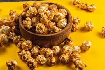 Sweet caramelized popcorn in a wooden bowl on a yellow background