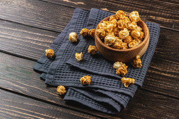 Snack, movie concept, caramelized popcorn in a wooden bowl on a wooden table