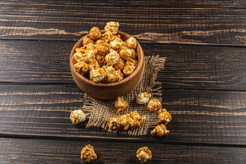 Snack, movie concept, caramelized popcorn in a wooden bowl on a wooden table