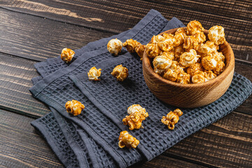 Snack concept, caramelized popcorn in a wooden bowl on a gray, wooden background