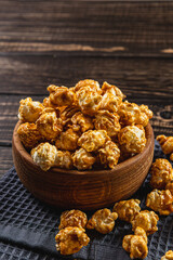 Snack concept, caramelized popcorn in a wooden bowl on a gray, wooden background
