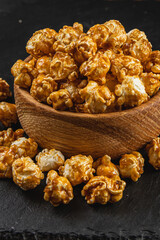 Snack concept, sweet caramelized popcorn in a wooden bowl on a black background