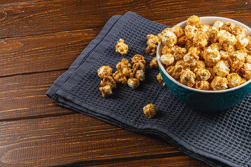 Snack concept, caramelized popcorn in a ceramic bowl on a wooden background