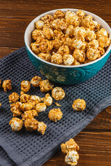 Snack concept, caramelized popcorn in a ceramic bowl on a wooden background