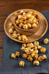 Caramelized popcorn in a wooden bowl with a plate on a wooden background
