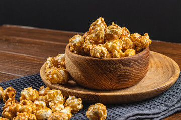Caramelized popcorn in a wooden bowl with a plate on a wooden background