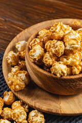 Caramelized popcorn in a wooden bowl with a plate on a wooden background