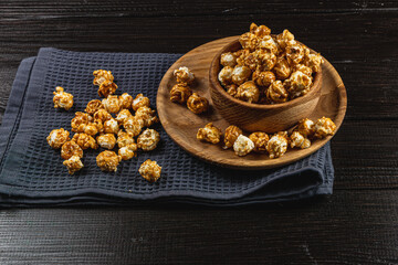 Caramelized popcorn in a wooden bowl with a plate on a wooden background
