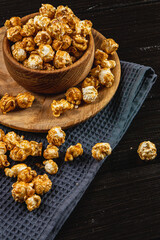 Caramelized popcorn in a wooden bowl with a plate on a wooden background
