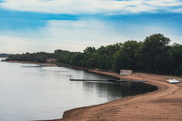 A quiet sandy beach with calm waters and a tree-lined shore, offering a peaceful and scenic view...