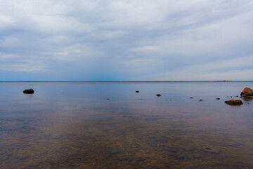 A tranquil seascape with calm water and scattered rocks beneath a cloudy sky, capturing the...