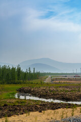 A remote construction site with a dirt road leading into the distance, surrounded by vegetation and...