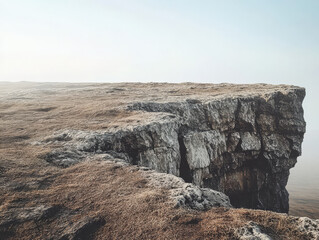 Obraz premium Rugged cliff edge overlooking foggy landscape at dawn with soft light illuminating terrain