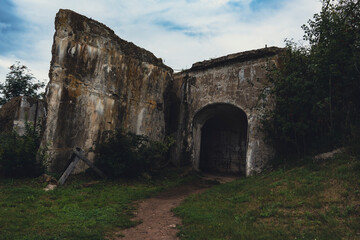 An abandoned stone fortress with weathered walls and an arched entrance, set in a grassy area,...