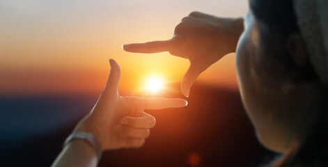 Close up of female hands making frame gesture view distant over sunset. Future planning idea concept.