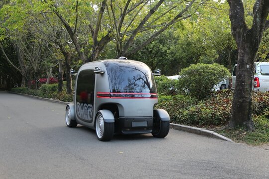 The small electric vehicle is parked on the side of an outdoor road, with a gray body color and black windows