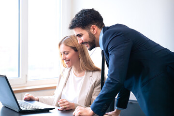 Fototapeta premium Professional man and woman working together on a laptop in a modern office. The woman points at the screen, explaining details while the man listens attentively.