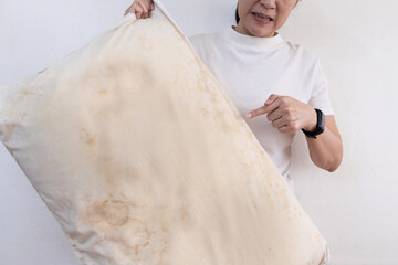 Old pillow with yellow and dirty stains,woman holding a dirty pillow and pointing at spots with...