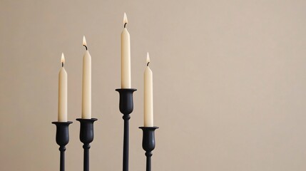 Minimalist candlesticks in black iron, holding ivory candles, set against a soft beige backdrop